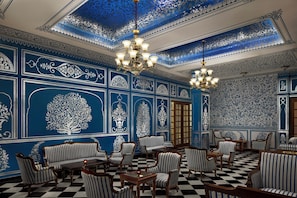 A room with ornate blue and white wall designs, black and white checkered flooring, and striped upholstered furniture.