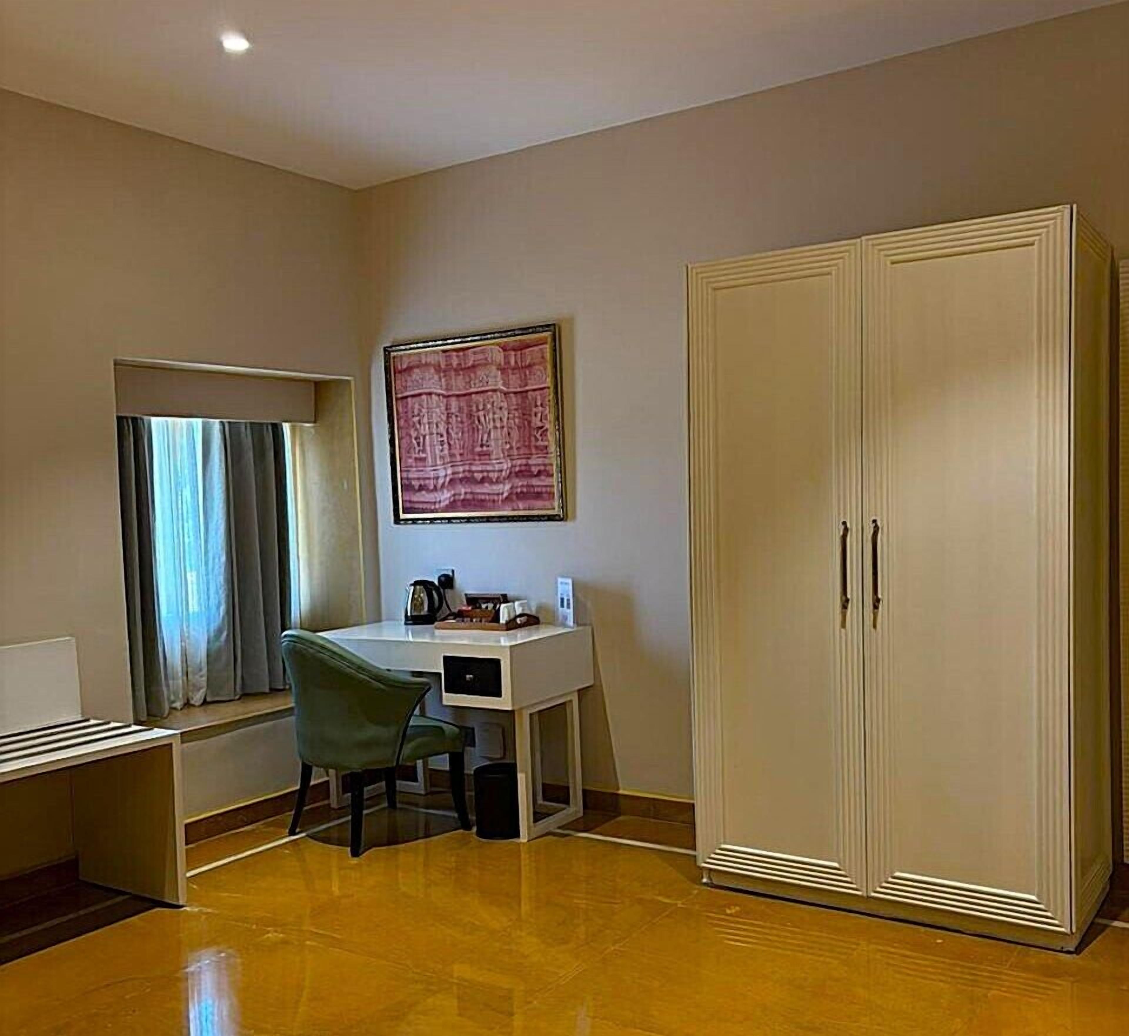 A room with a desk, chair, wardrobe, and a painting on the wall.