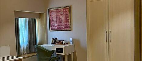 A room with a desk, chair, wardrobe, and a painting on the wall.