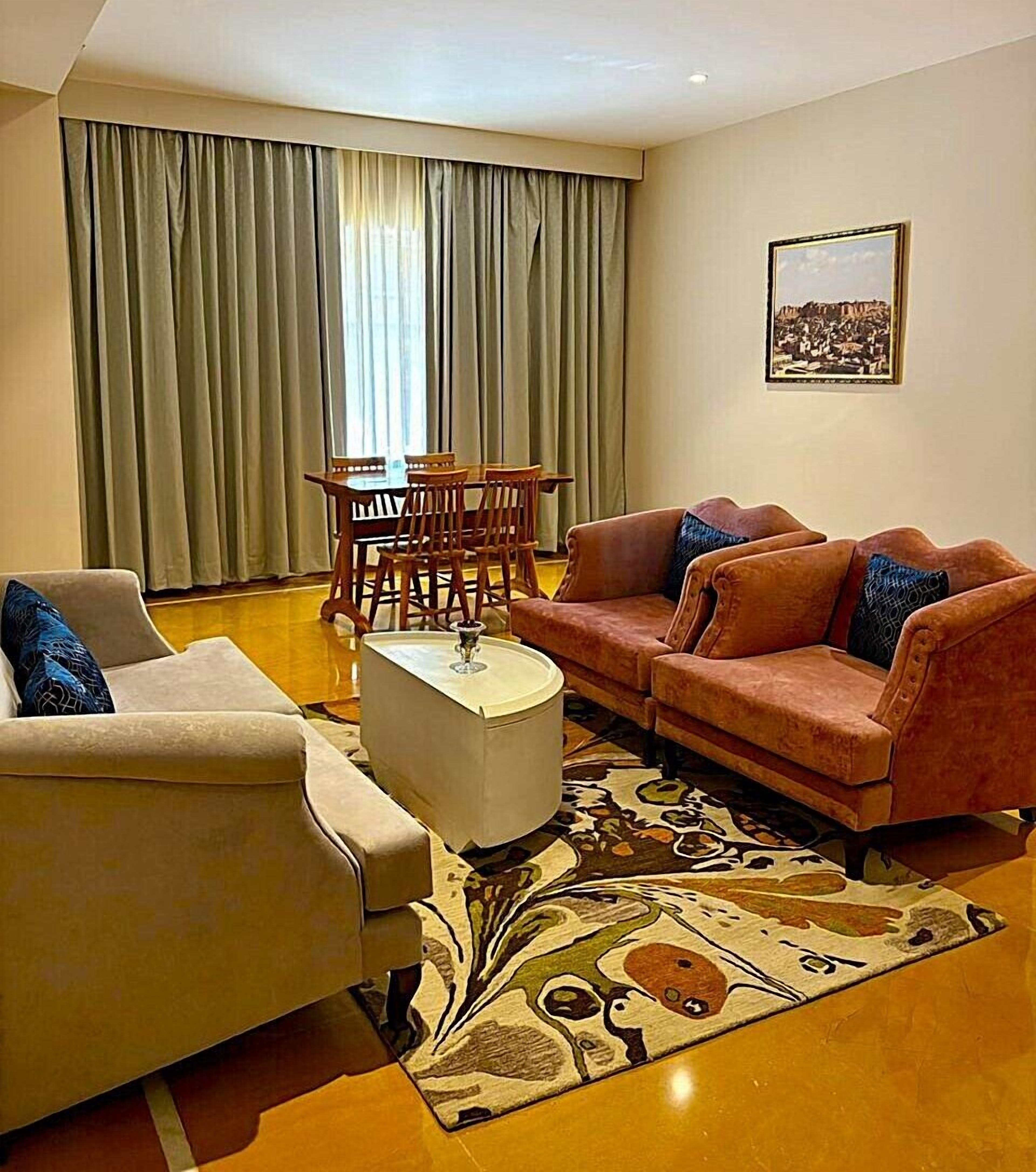 A living room with a sofa, armchair, coffee table, and a dining table with chairs.