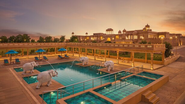 Zona de piscina con estatuas de elefantes, un puente y un edificio grande al fondo.