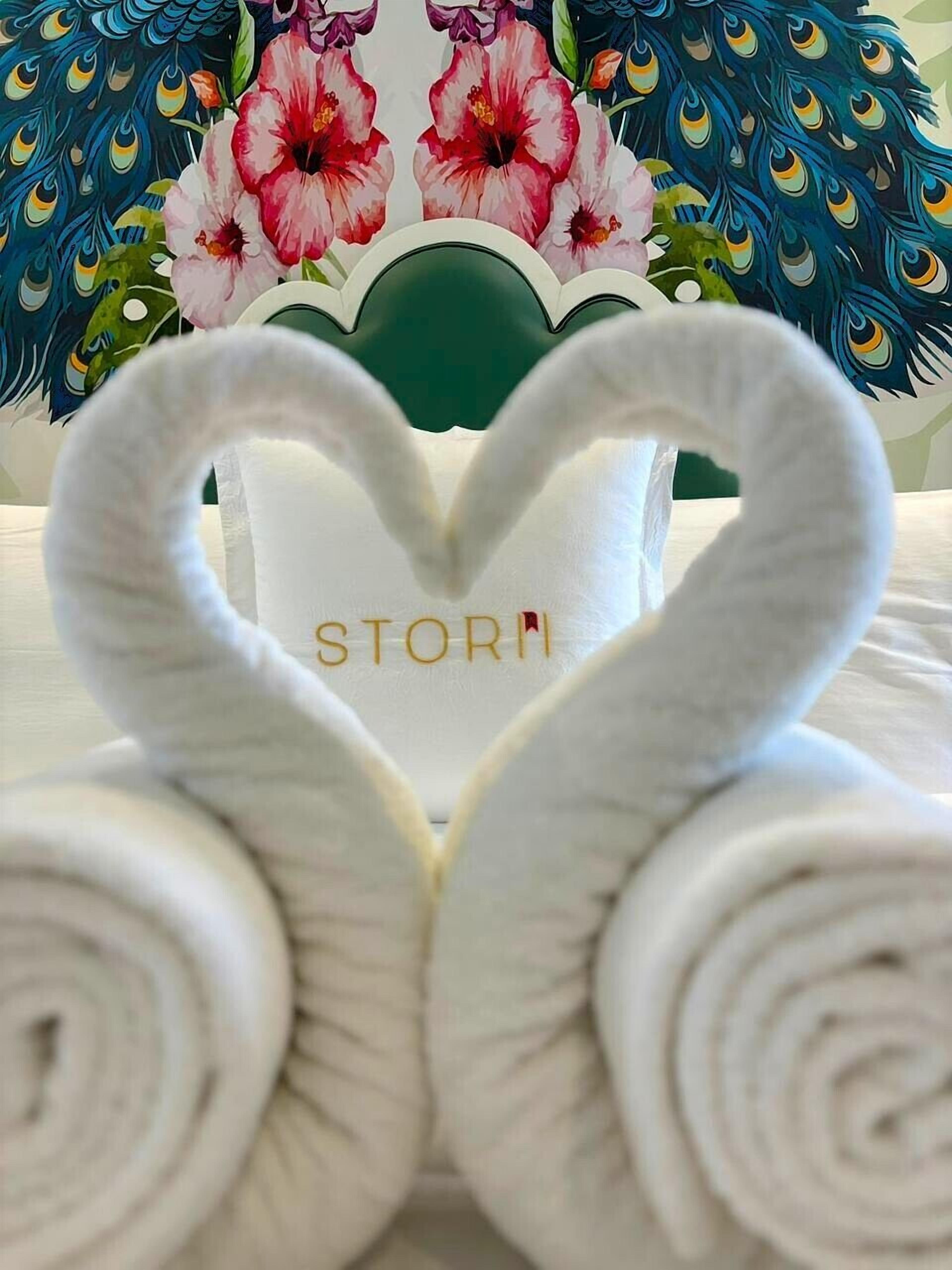 A bed with a heart-shaped towel arrangement and a pillow with the word "STORY" on it.