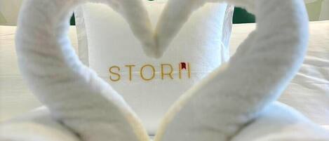A bed with a heart-shaped towel arrangement and a pillow with the word "STORY" on it.