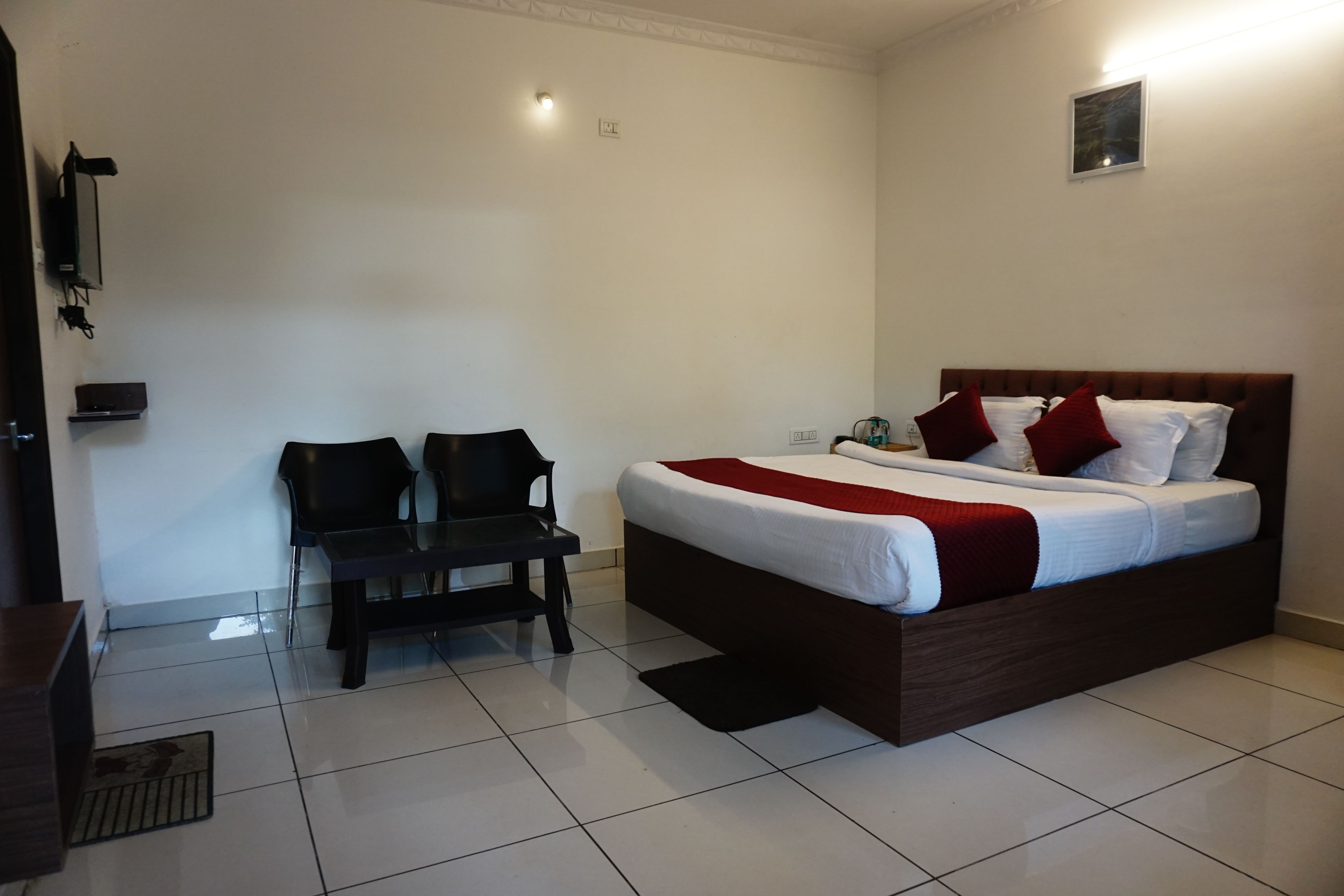 A hotel room with a bed, two chairs, a small table, and a wall-mounted TV.