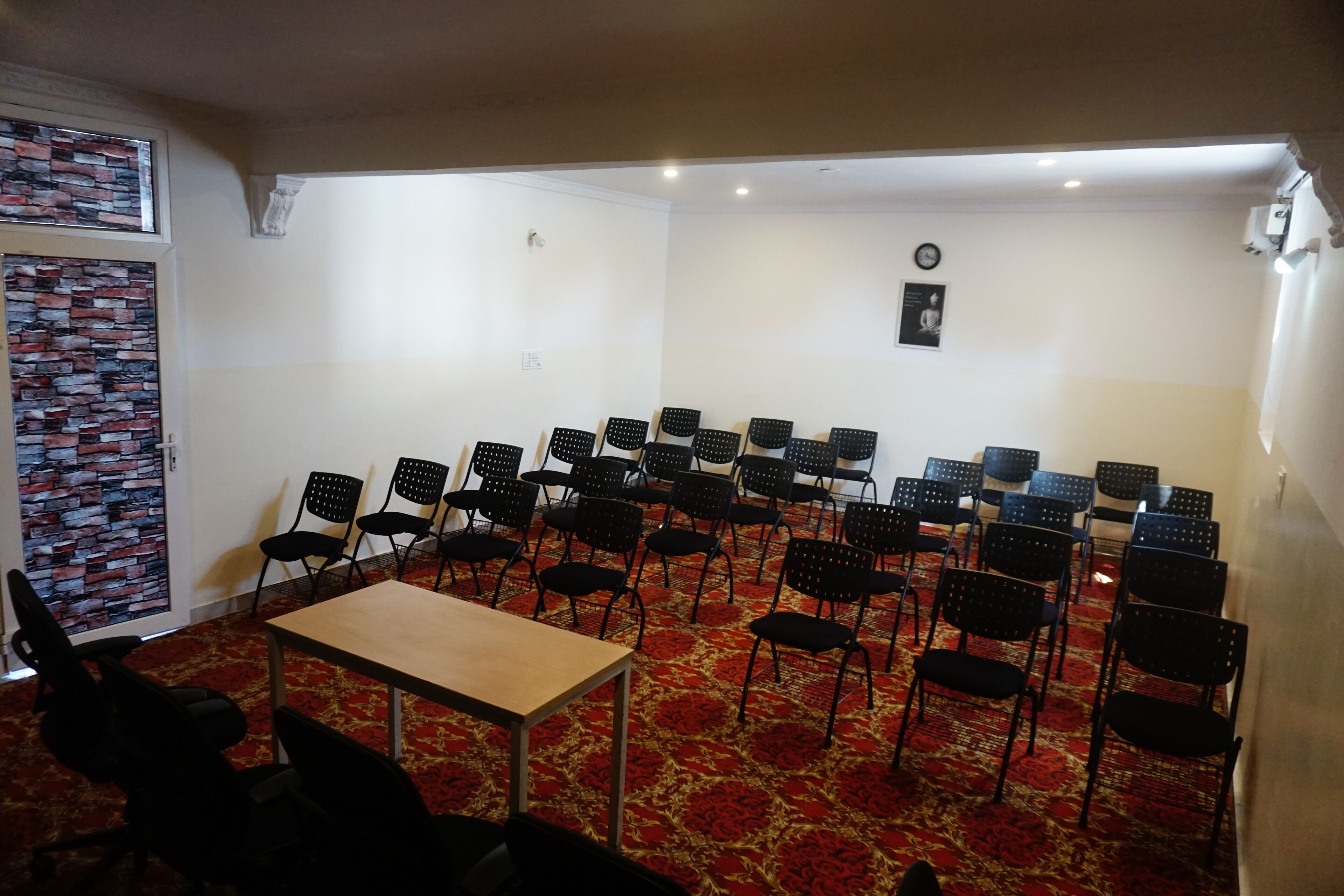 A conference room with a carpeted floor, a wooden table, and rows of black chairs.