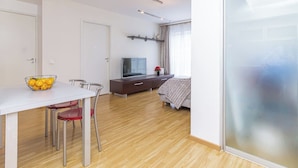 Een moderne woonkamer met een eethoek, een flatscreen televisie en een bed met een geborduurde deken.