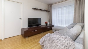 Een moderne woonkamer met een flatscreen televisie, een bank, een houten vloer en een raam met gordijnen.