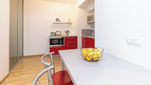 Een moderne keuken met een wit aanrecht, rode kastjes en een schaal fruit op de tafel.