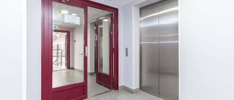 A hallway with a red door, a glass door, and a metallic elevator.