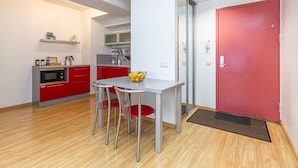 Een kleine keuken met rode kastjes, een wit aanrechtblad en een eethoekje met twee stoelen en een tafel.