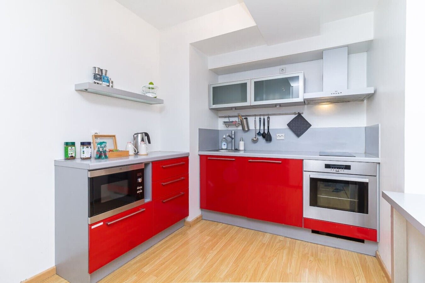 A compact kitchen with red cabinets, a microwave, and a built-in oven.