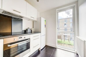 A modern kitchen with a built-in oven, a toaster, and a refrigerator. There is a sliding glass door leading to a balcony with a view of a building and a grassy area. - London Apartment next to tube station (London)