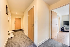 A hallway with carpeted floors, wooden doors, and a visible TV in the adjacent room.