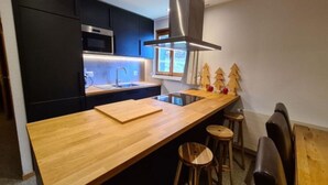 A modern kitchen with dark cabinetry, a wooden countertop, a stainless steel range hood, and a window with a view. - Apartment With Panoramic Views (Veysonnaz)