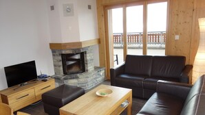 A cozy living room with a stone fireplace, leather sofa, wooden coffee table, and a flat-screen TV. - Apartment With Panoramic Views (Veysonnaz)