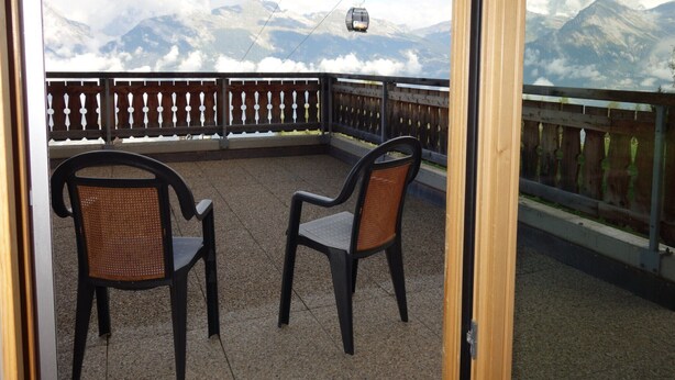 A balcony with two wicker chairs, a wooden fence, and a mountain view with a cable car in the distance. - Apartment With Panoramic Views (Veysonnaz)
