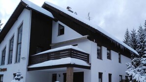 Un edificio moderno su due piani con un balcone e un ingresso coperto, circondato da alberi innevati.