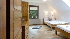 Une chambre avec deux lits, une armoire en bois, un puits de lumière et une fenêtre donnant sur un paysage verdoyant.