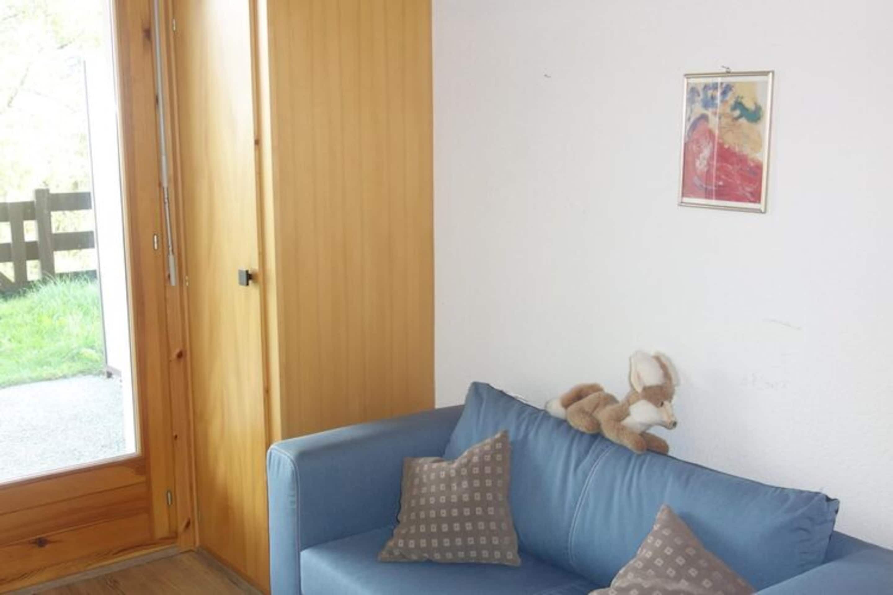 A room with a wooden door, a blue sofa with patterned cushions, and a framed picture on the wall.