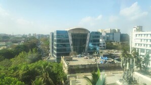 A modern building with a curved glass facade, surrounded by greenery and other buildings. - Glitz Hotels Aksha International (Mumbai)