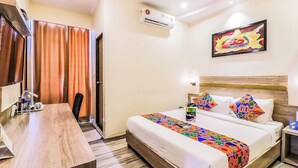 A hotel room with a bed, a desk, a chair, an air conditioning unit, and a painting on the wall. - Glitz Hotels Aksha International (Mumbai)