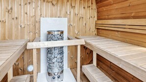 Una sauna de madera con bancos y un calentador central de piedra.
