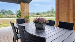Un área de comedor al aire libre con mesa y sillas de madera, rodeada de pilares de madera y con vistas a un paisaje natural.