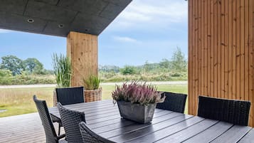 Um pátio externo com mesa e cadeiras de madeira, cercado por painéis verticais, com vista para uma paisagem natural.