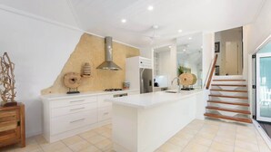 A modern kitchen with a central island, white cabinetry, and a wooden staircase. - Villa 5 on Murphy - Spacious Living, Walk to Town (Port Douglas)