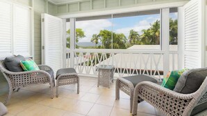 A balcony with wicker furniture, a small table, and a view of palm trees and the ocean. - Villa 5 on Murphy - Spacious Living, Walk to Town (Port Douglas)