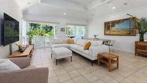 A spacious living area with a large sectional sofa, a wooden coffee table, and a flat-screen TV mounted on the wall. - Villa 5 on Murphy - Spacious Living, Walk to Town (Port Douglas)
