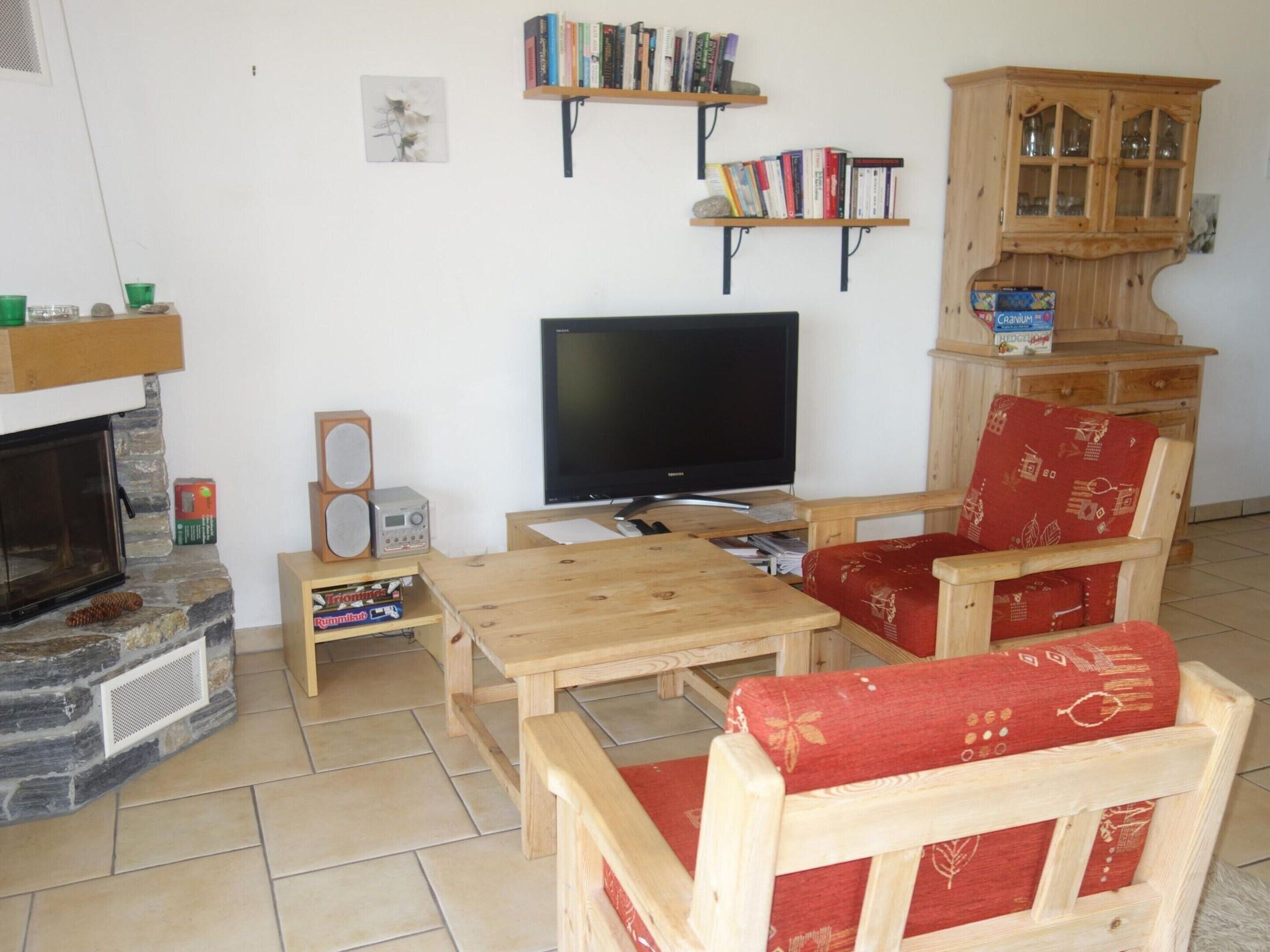 A cozy living room with a fireplace, a television, wooden furniture, and bookshelves.