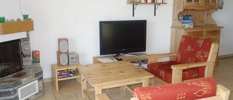 A cozy living room with a fireplace, a television, wooden furniture, and bookshelves.