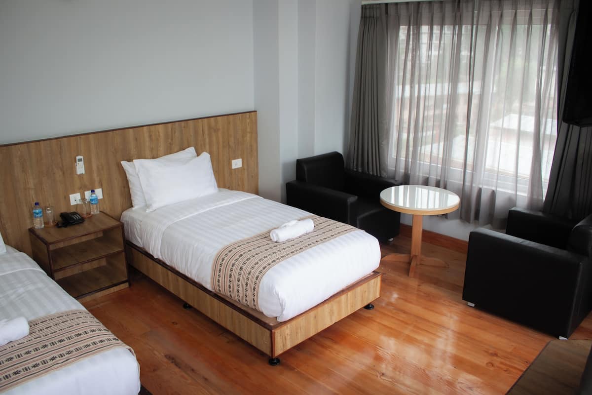 A hotel room with a wooden bed, a small bedside table with a phone and water bottles, a round table, and two black chairs.
