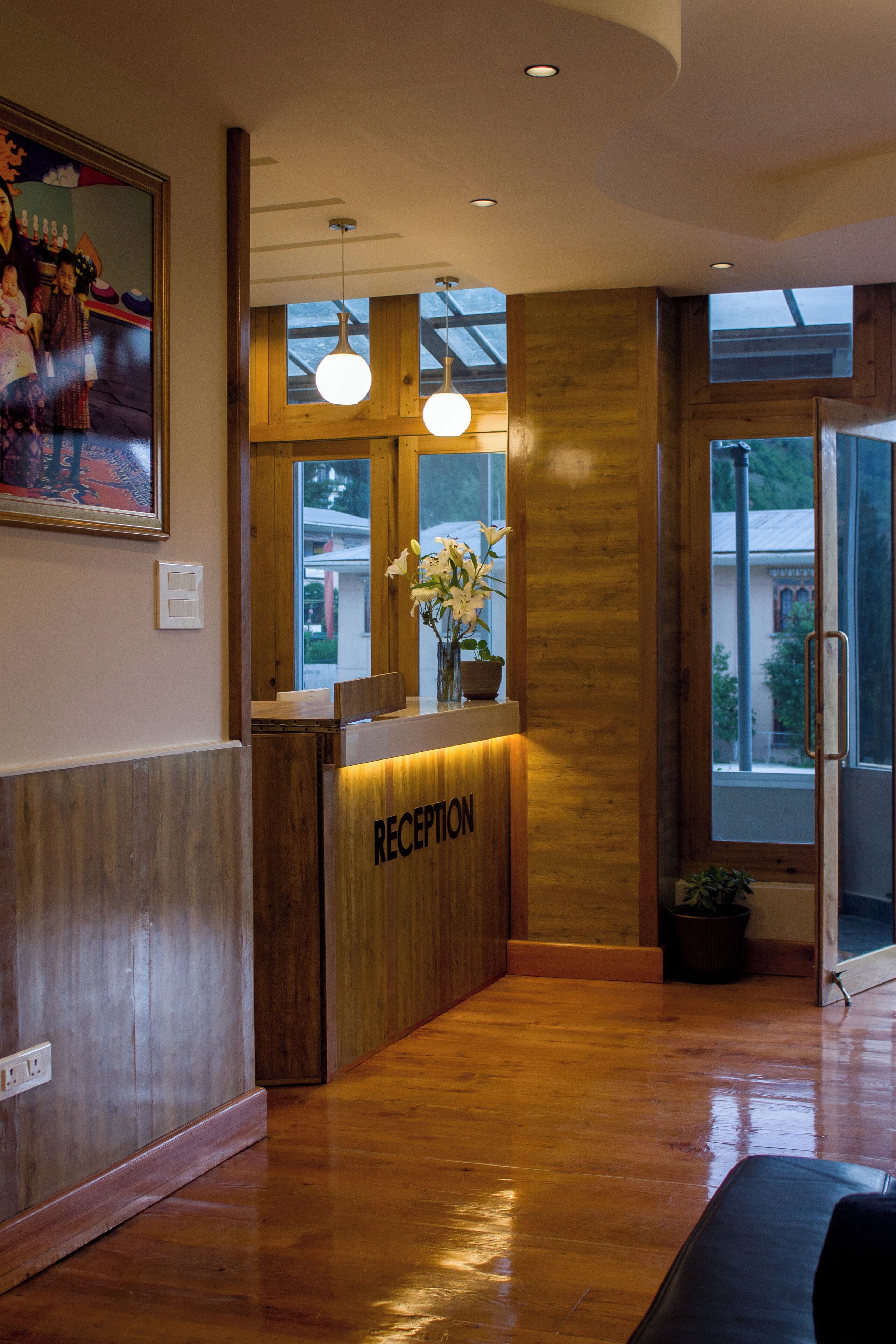 Una zona de recepción con un mostrador de madera, un jarrón con flores y un cuadro en la pared.