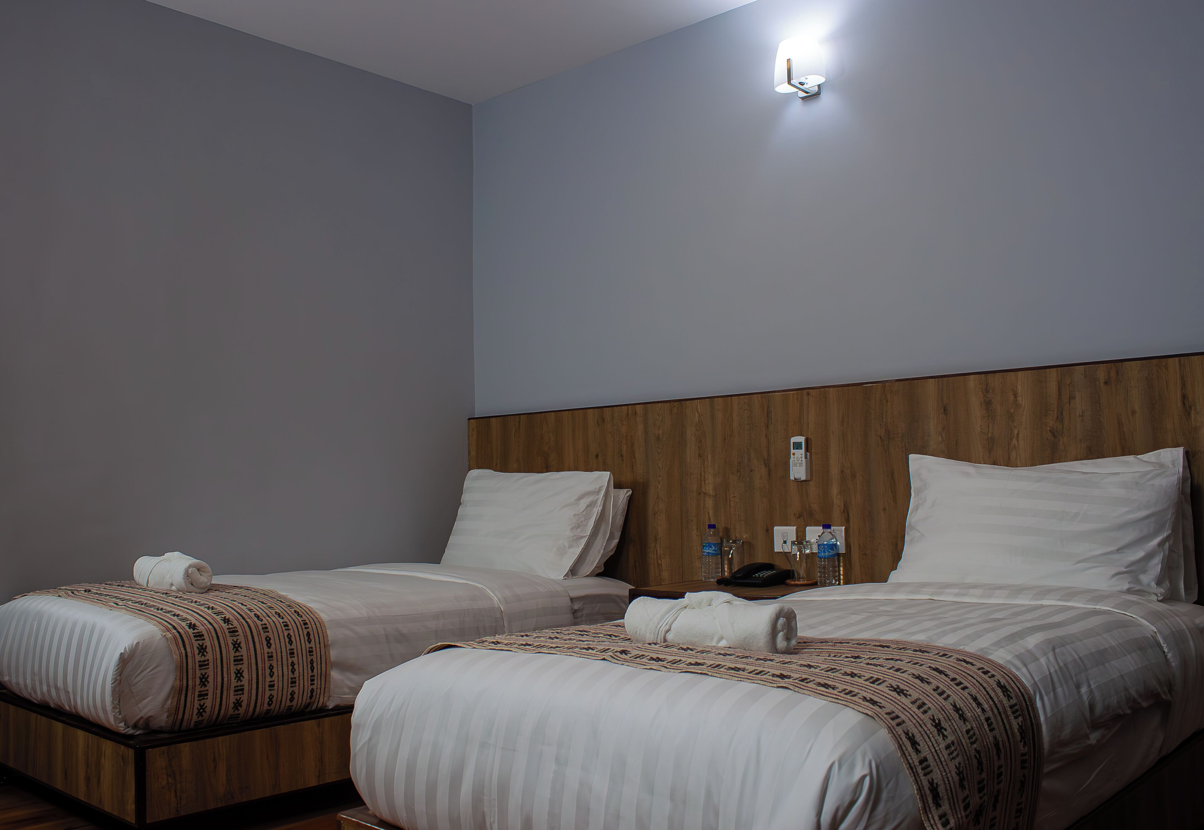 Een hotelkamer met twee bedden, houten hoofdborden en een nachtkastje met een telefoon en waterflessen.