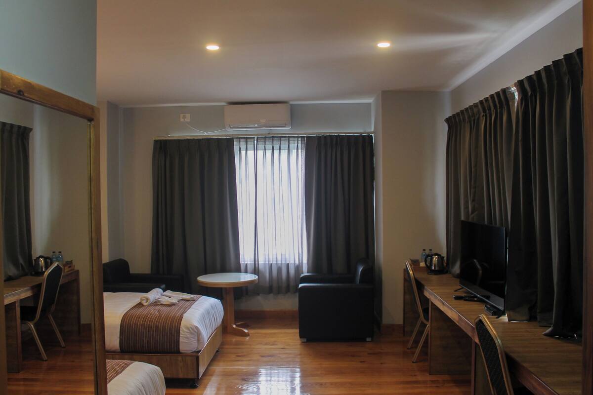 A hotel room with a bed, a desk, a chair, a television, and a window with curtains.