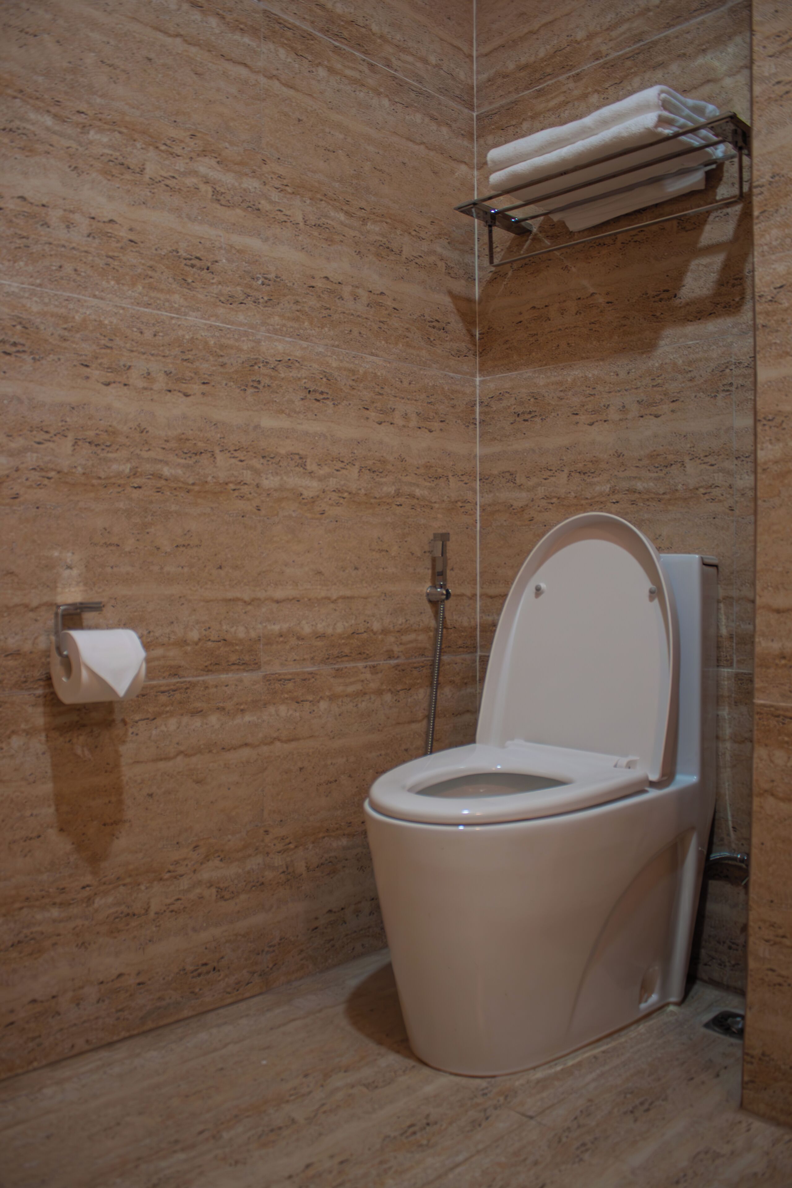 A bathroom with a marble wall, a toilet, a towel rack, and a toilet paper holder.