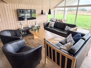 A modern living room with a wooden floor, leather sofas, a coffee table, and a flat-screen TV mounted on the wall.