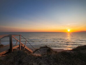A sunset over the ocean with a wooden staircase leading down to the beach.