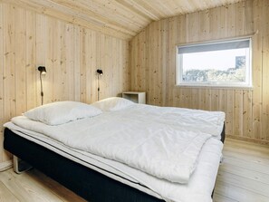 A bedroom with a bed, two bedside lamps, a window, and wooden walls.