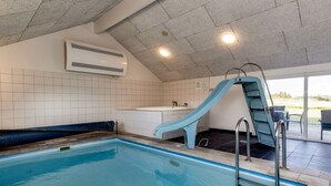 En swimmingpool med en blå vattenrutschkana, en vit kakelbeklädd vägg och ett tak med infälld belysning.