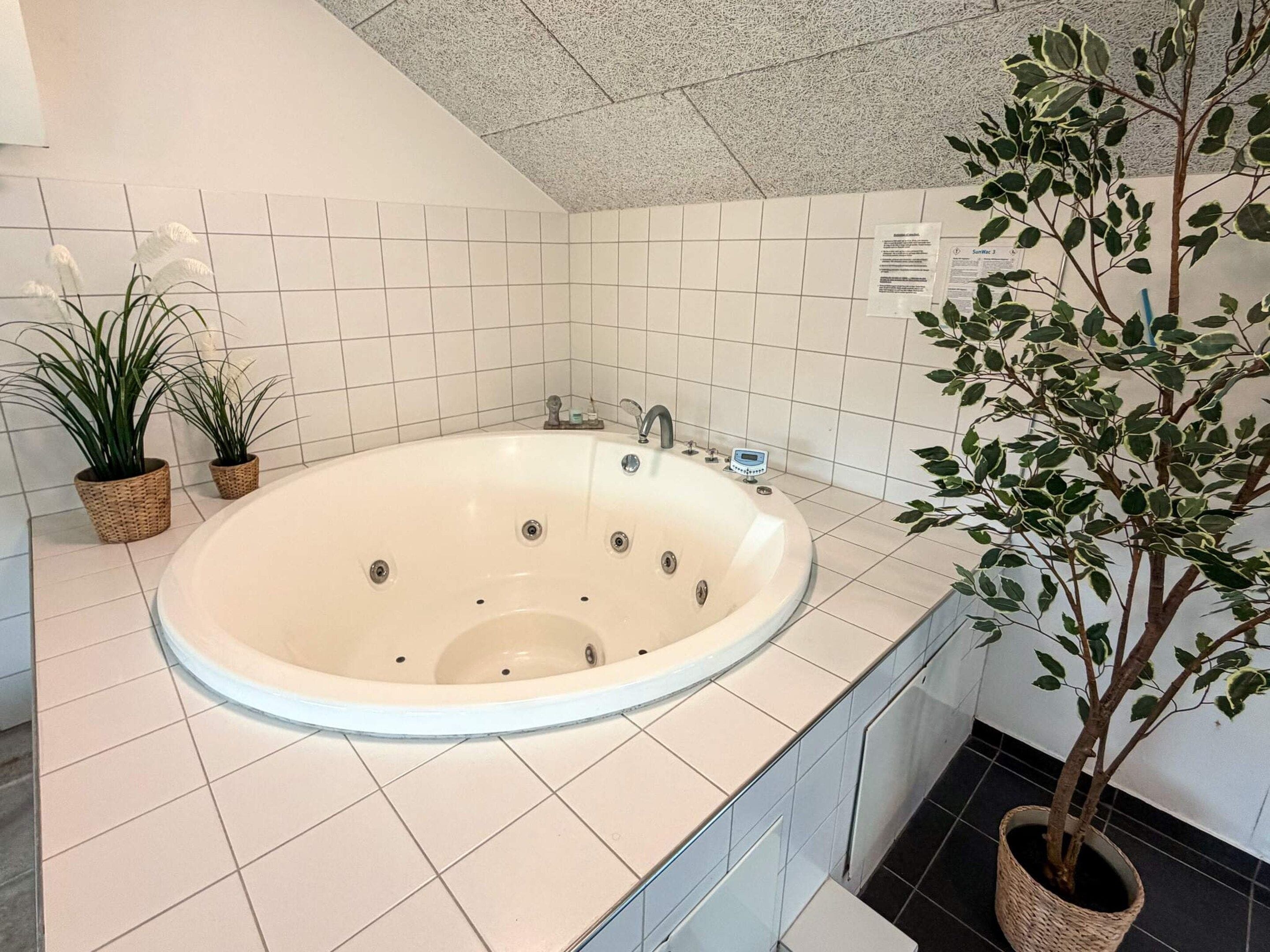 Ett badrum med ett fristående badkar, vita kaklade väggar och en krukväxt.