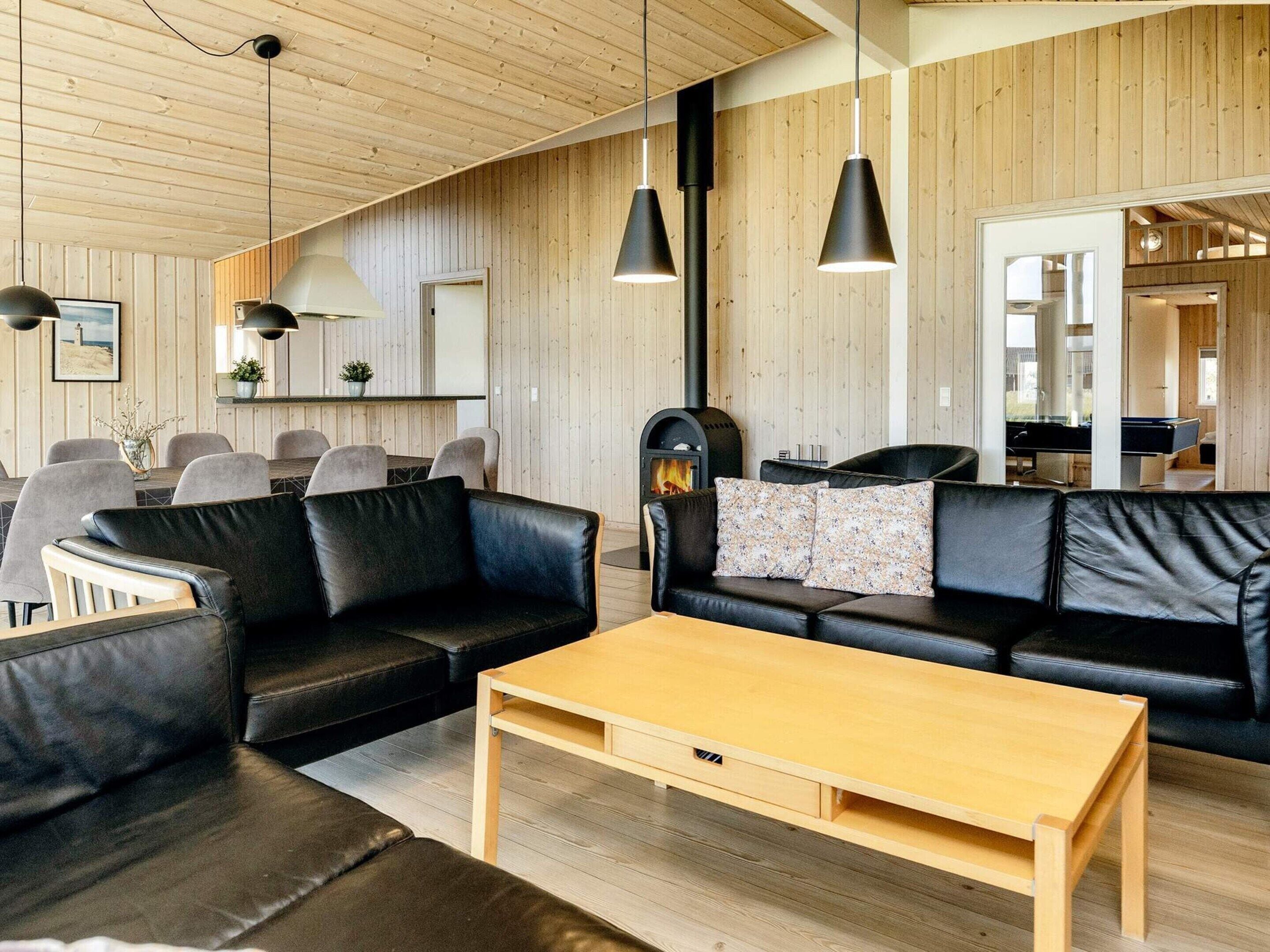 A modern living room with a wooden ceiling, black leather sofas, a wooden coffee table, and pendant lighting.