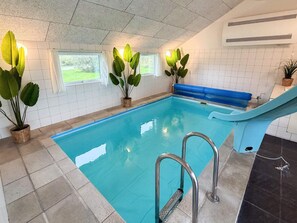 Piscina interna com água cristalina, paredes azulejadas e plantas em vasos.
