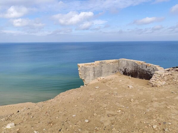 Un paysage côtier avec une structure en béton, un terrain sablonneux et une vue dégagée sur la mer.