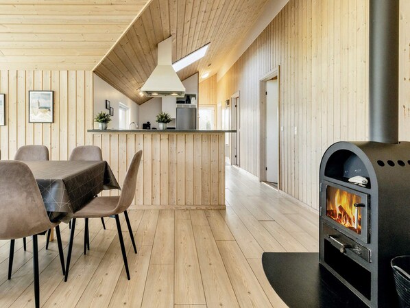 A modern interior with a wooden floor, a dining area with chairs, a kitchen with a stove, and a fireplace.