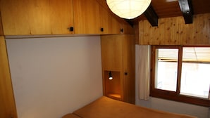 Une pièce avec un lit, des murs en bois, une fenêtre et un luminaire au plafond.