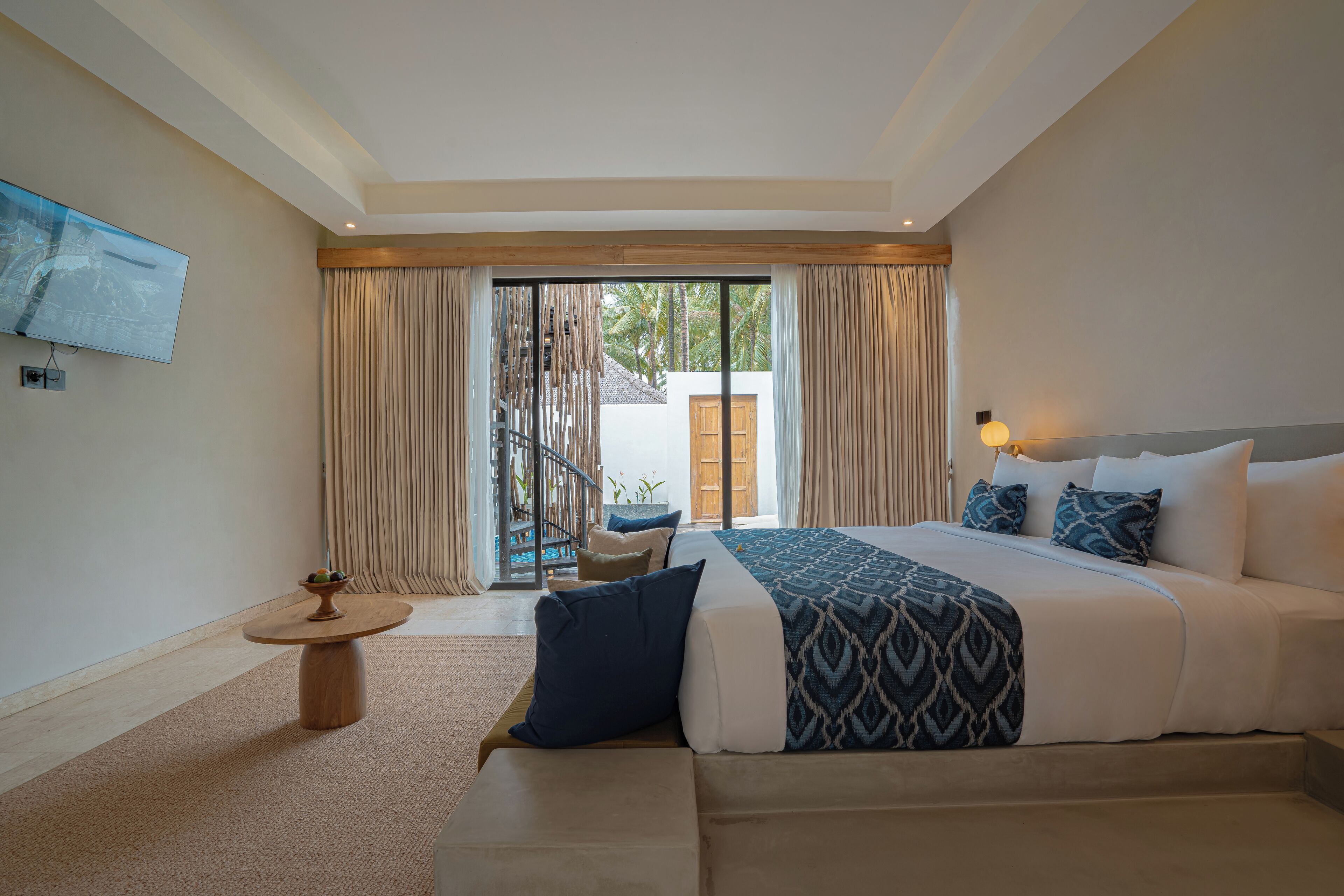 A hotel room with a large bed, a TV mounted on the wall, and a balcony with curtains.