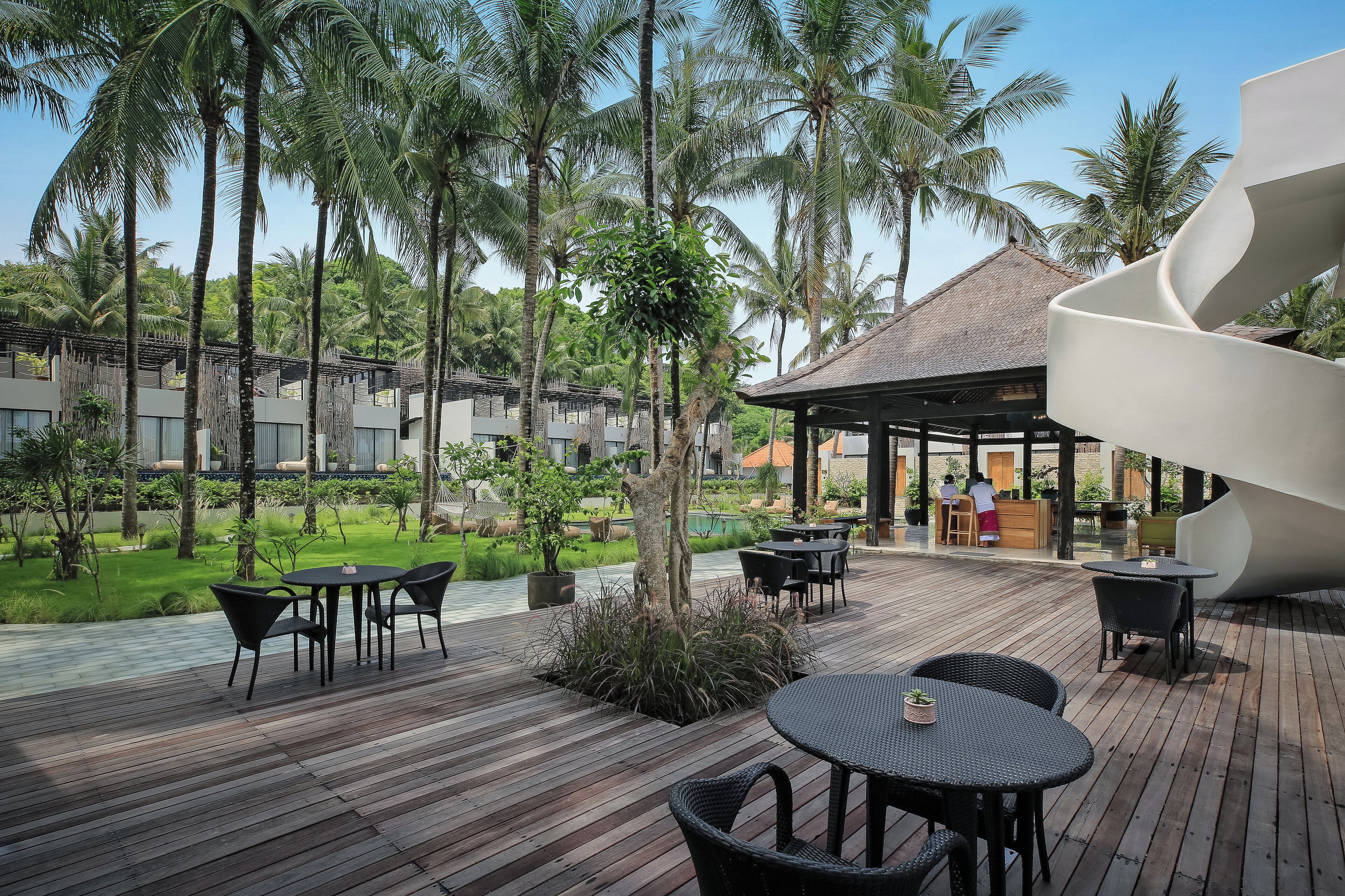 A wooden deck with outdoor seating, surrounded by lush greenery and palm trees.